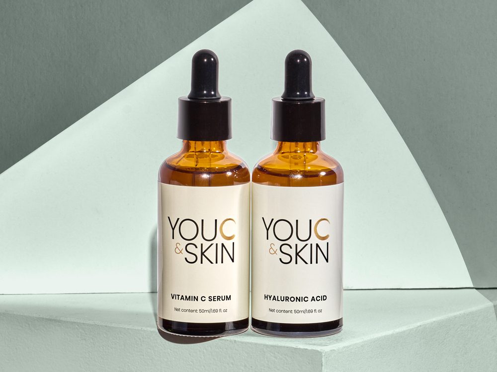 Two You C and Skin dropper bottles, Vitamin C Serum and Hyaluronic Acid, on a mint green backdrop